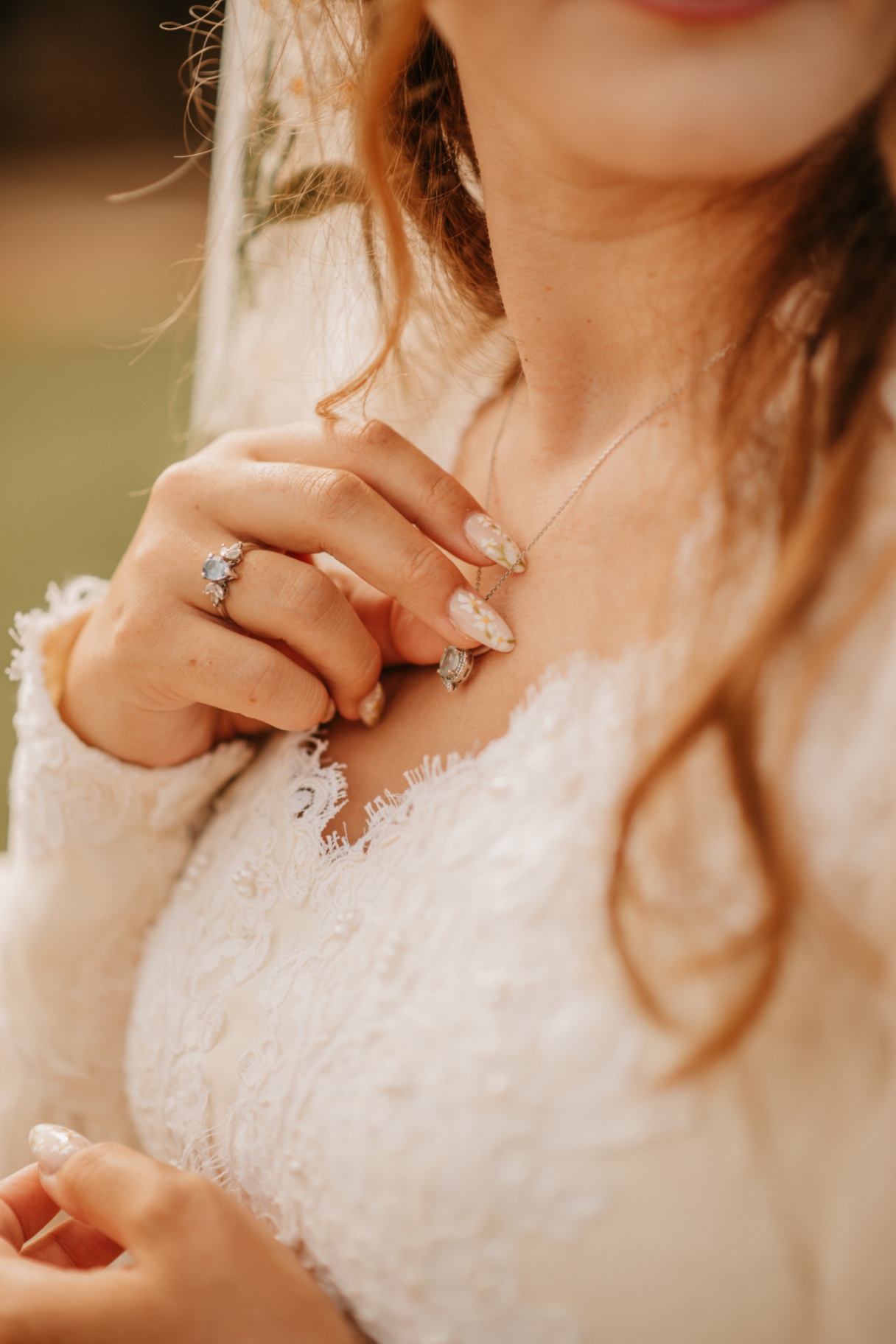 Close-up of the bride adjusting her delicate necklace over a lace gown