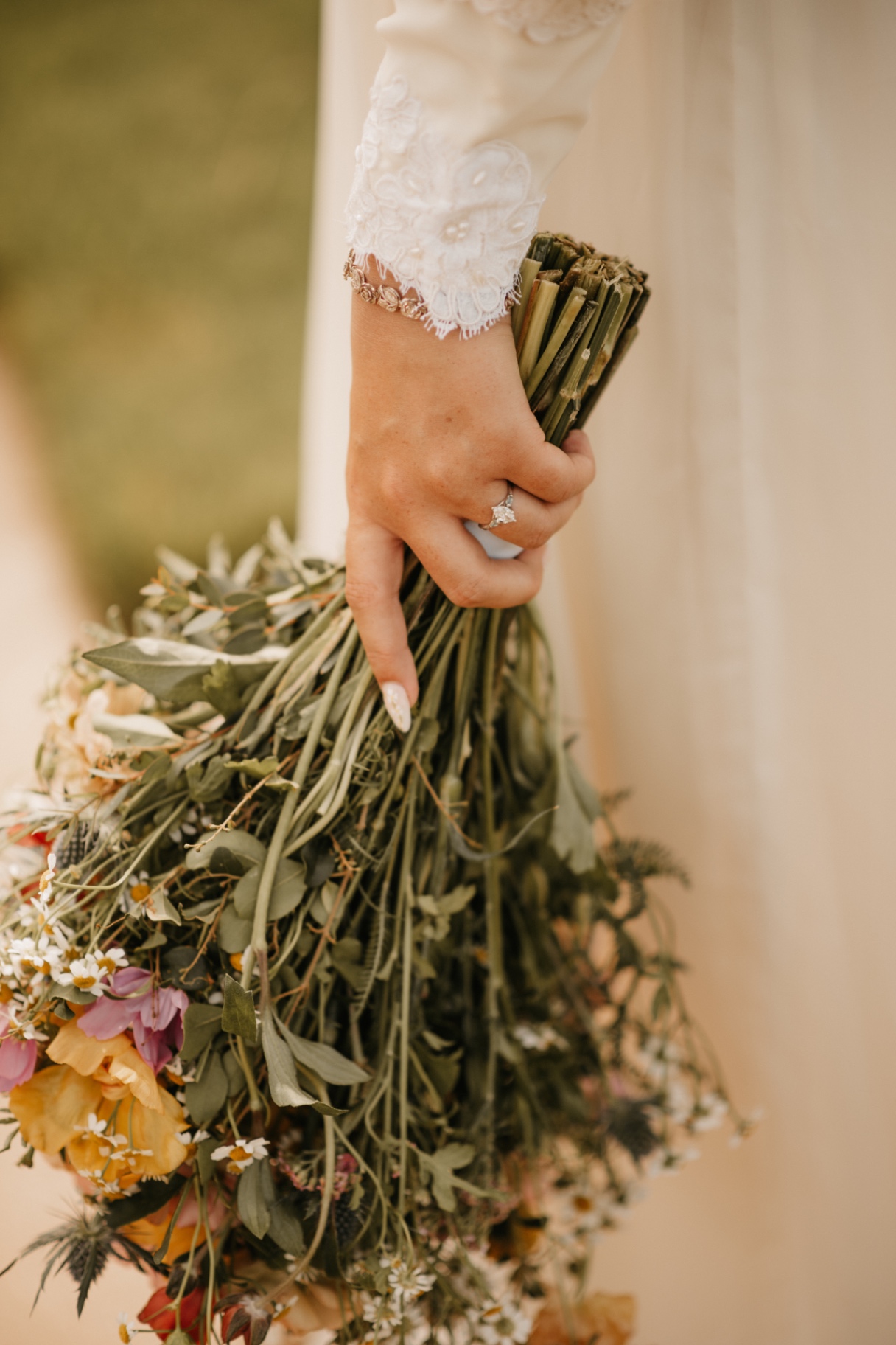 Detail of the bride's hand and engagement ring resting on a wildflower bouquet