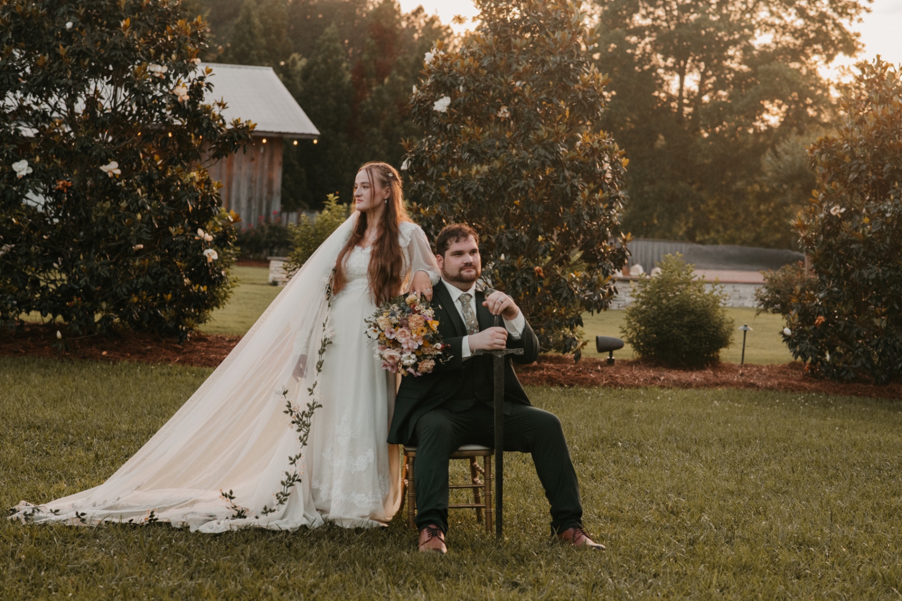 Storybook couple portrait at golden hour with sword and flowing veil in front of a magnolia