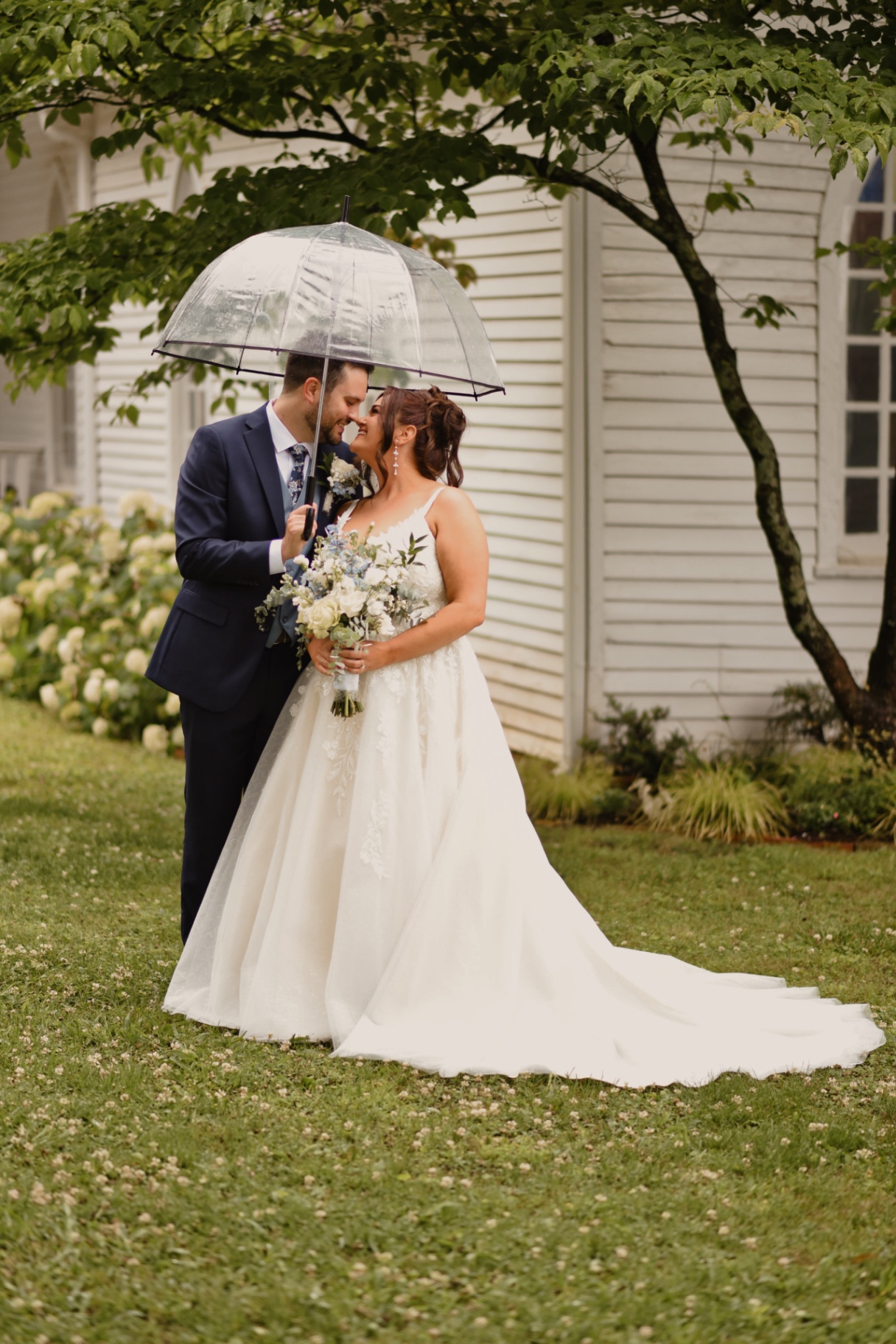 Bride and groom sharing a quiet moment beneath a clear umbrella on a rainy wedding day